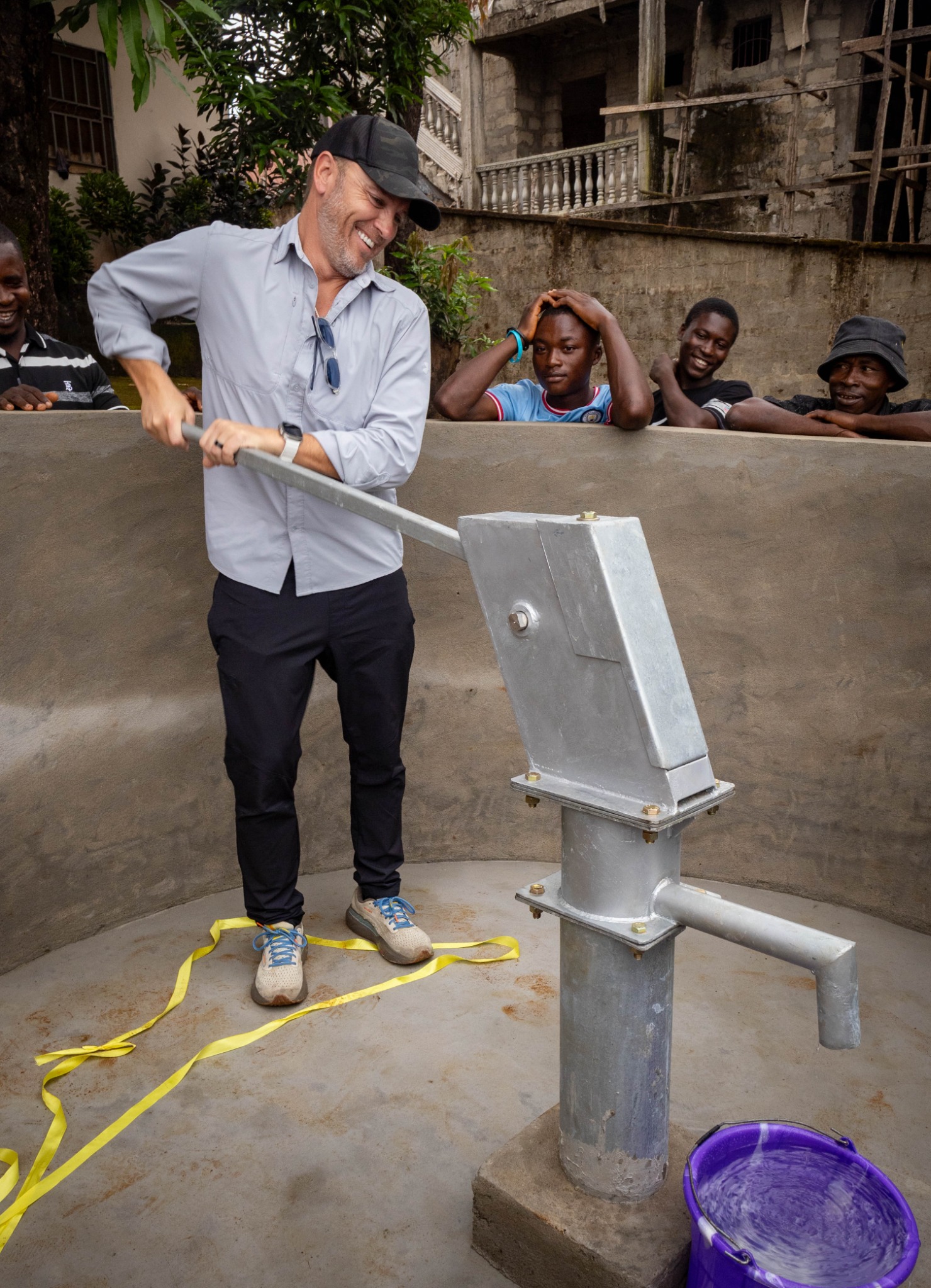 A WaterIsLife volunteer using a completed deep borehole water pump with community members in Sierra Leone